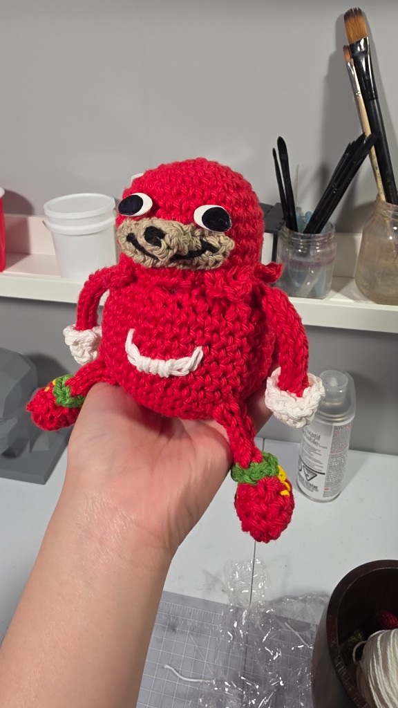 Hand holding a small crocheted plushie in a craft studio