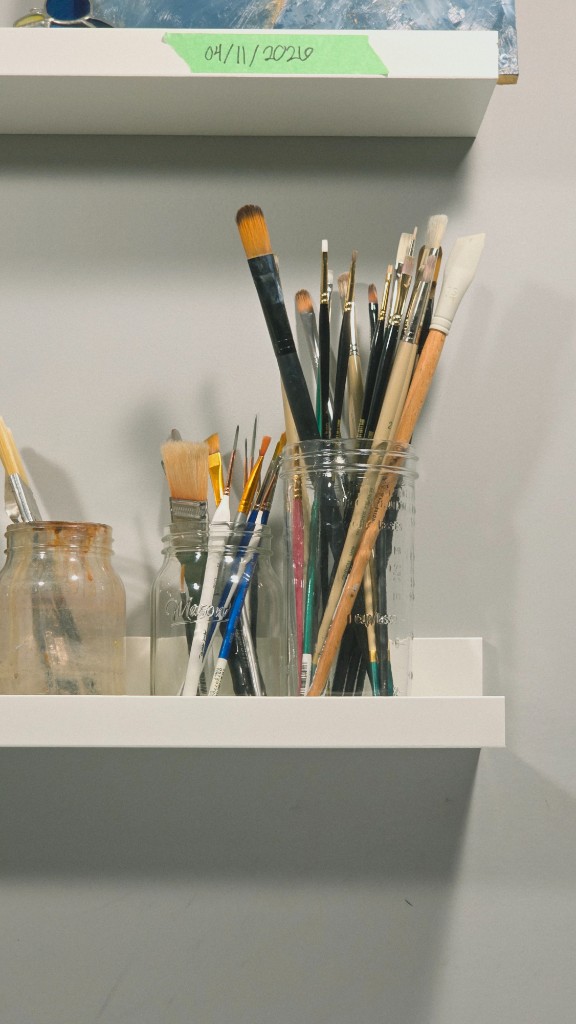 Paintbrushes in glass jars on a studio shelf